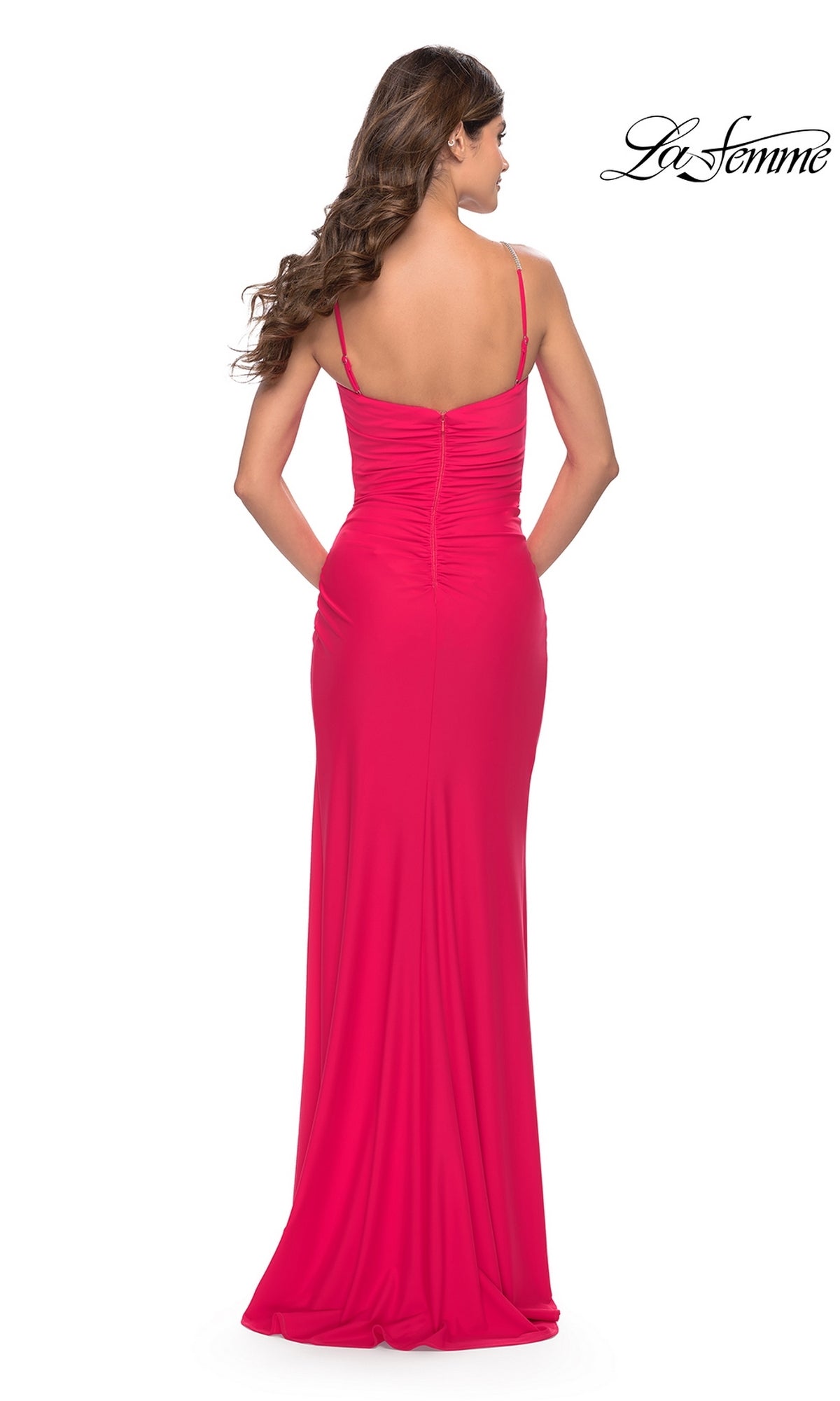 Woman seen from behind in the La Femme Hot Coral Pink Prom Dress 31224, a fitted, floor-length gown with thin straps and ruched back. The La Femme logo appears in the top right corner.